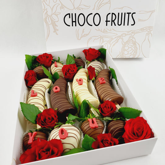 Choco Fruits Schokoerdbeeren und Schokobananen mit I Love You Buchstaben verziert und mit roten Rosen dekoriert
