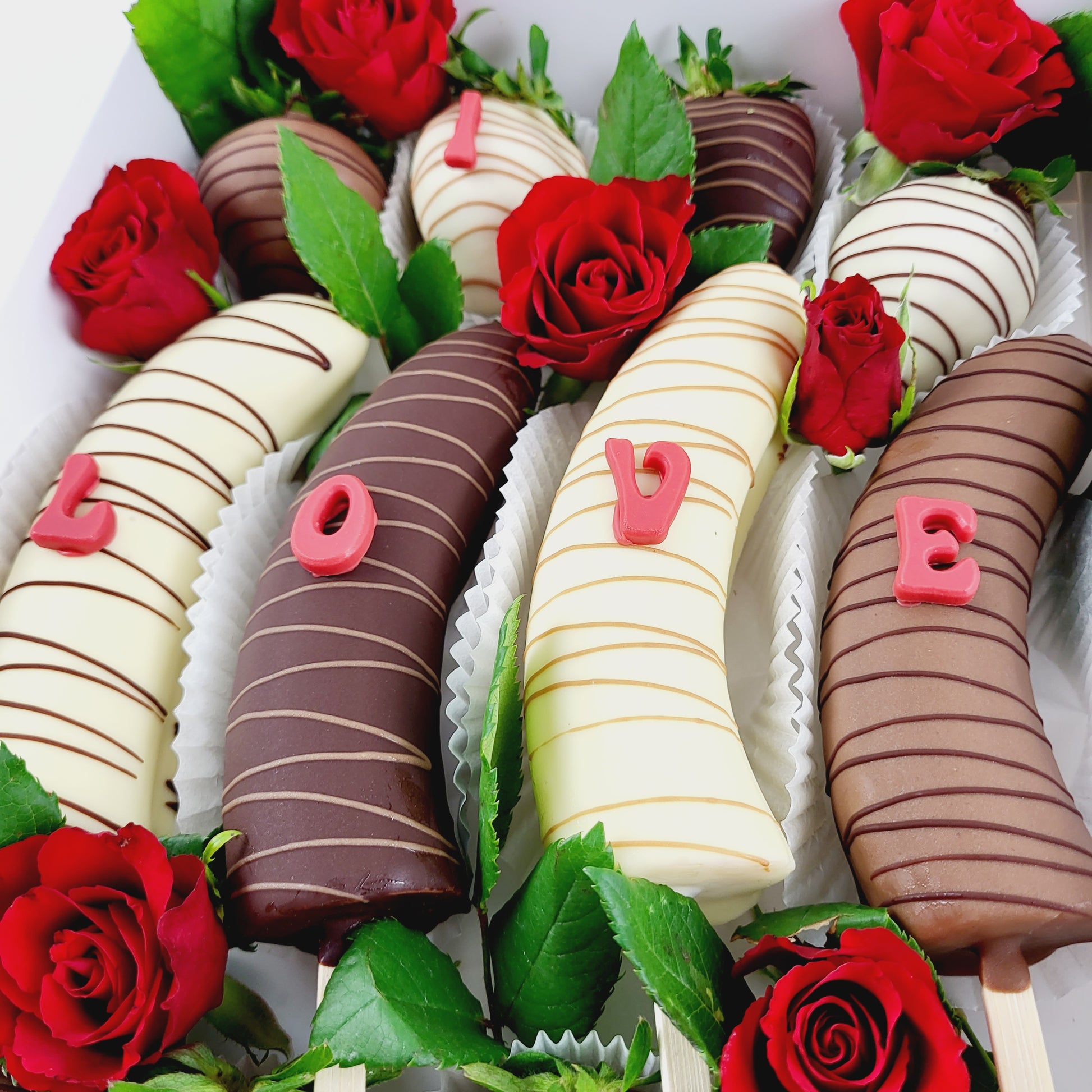 Choco Fruits Schokoerdbeeren und Schokobananen mit I Love You Buchstaben verziert und mit roten Rosen dekoriert
